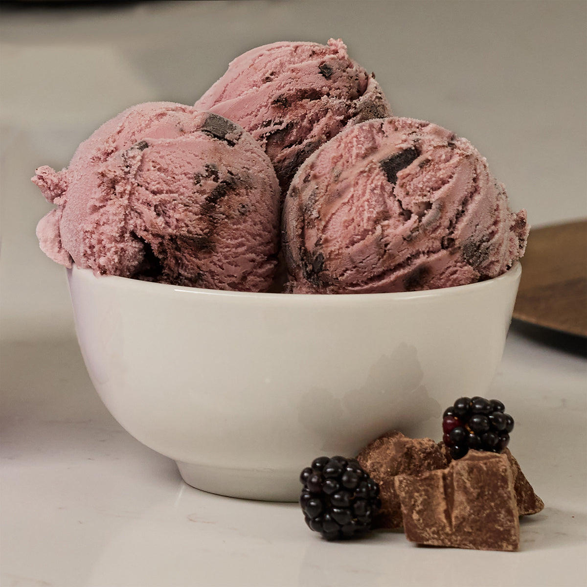 Blue Bell Black Raspberry Fudge Ice Cream in a white bowl with black raspberries and chocolate chunks