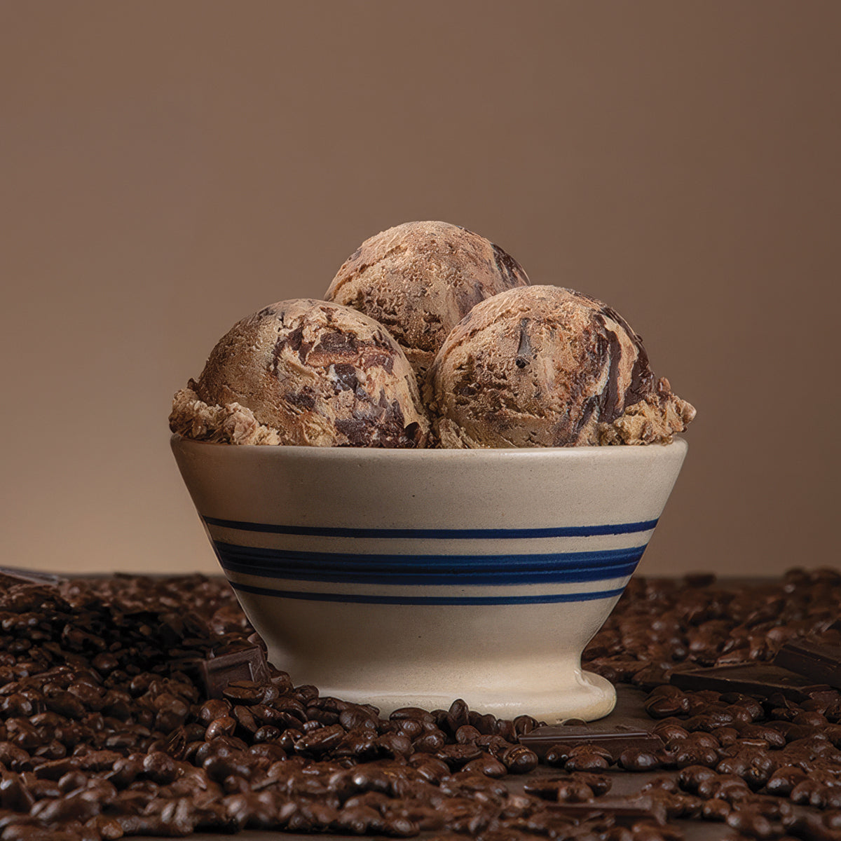 Bowl of Blue Bell Java Jolt Ice Cream with chocolate and coffee beans scattered in front with a brown background