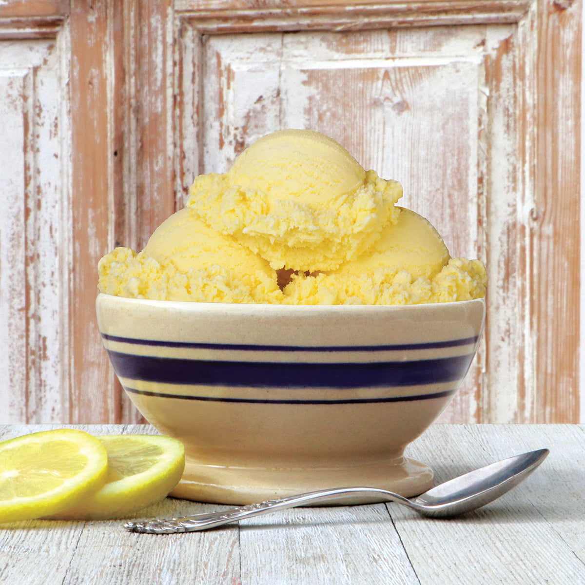 Bowl of Blue Bell Lemon Ice Cream with lemon slices and spoon in a rustic wooden setting.