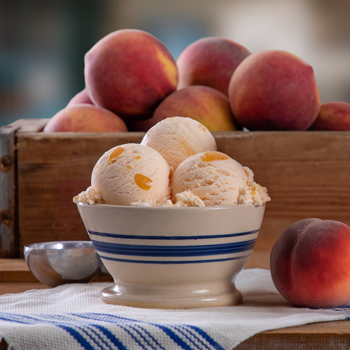 Bowl of Blue Bell Peaches and Homemade Vanilla Ice Cream with a crate of fresh peaches in the background.