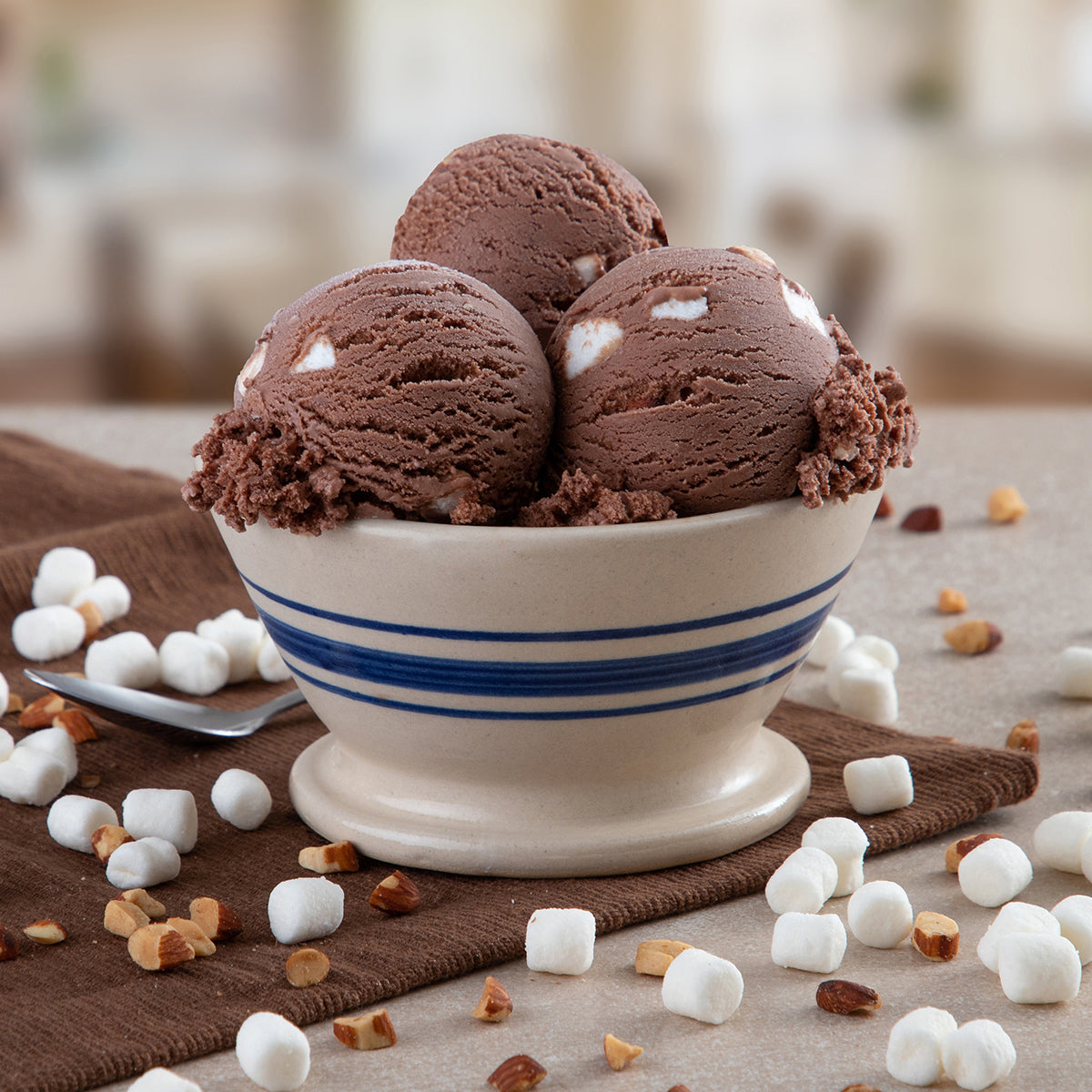 Bowl of Blue Bell Rocky Road Ice Cream on a brown towel with marshmallows and almonds scatted around. 