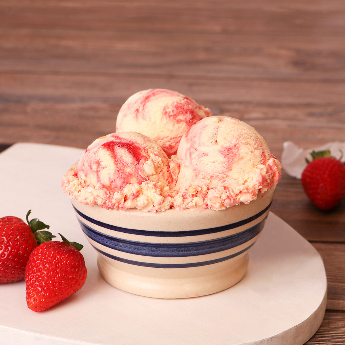 Bowl of Blue Bell Strawberry Cheesecake Ice Cream on a white serving platter and strawberries placed on a wooden table. 